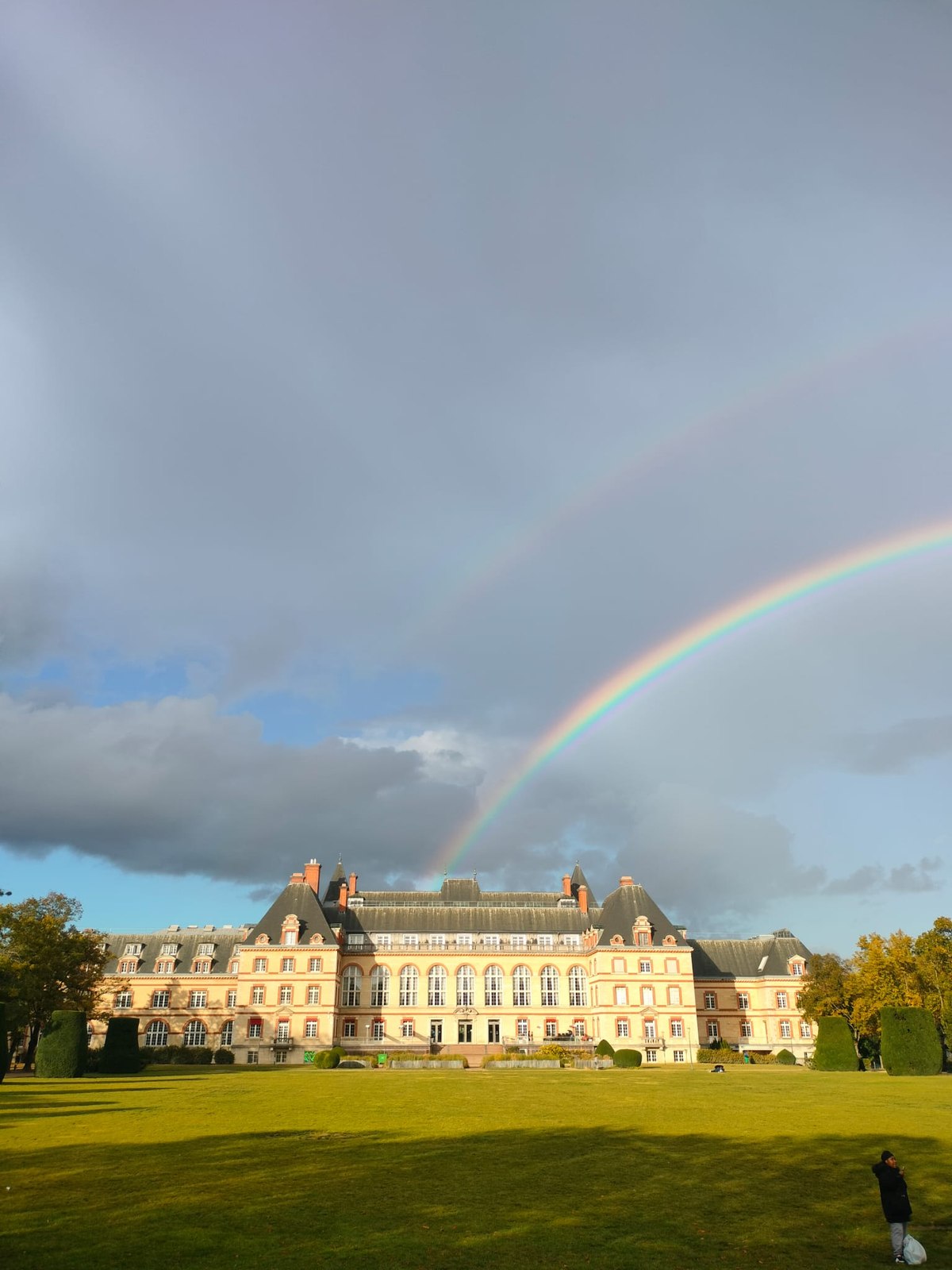 A rainbow over a grand building and lawn
