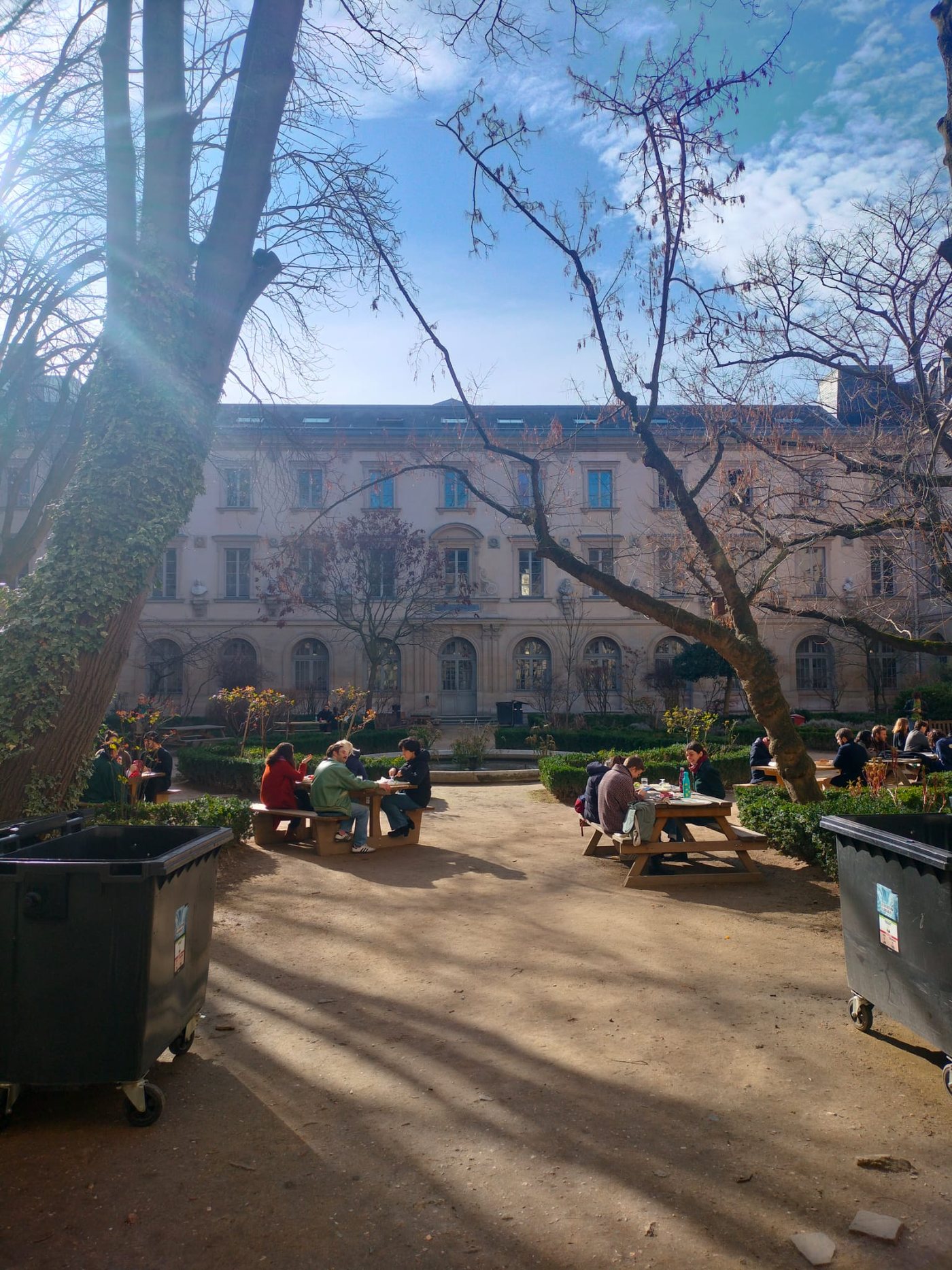 A sunlit courtyard with people at picnic tables